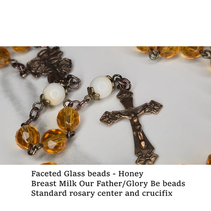 Rosary with honey-colored faceted glass beads, breast milk Our Father/Glory Be beads, standard rosary center, and crucifix on a marble surface