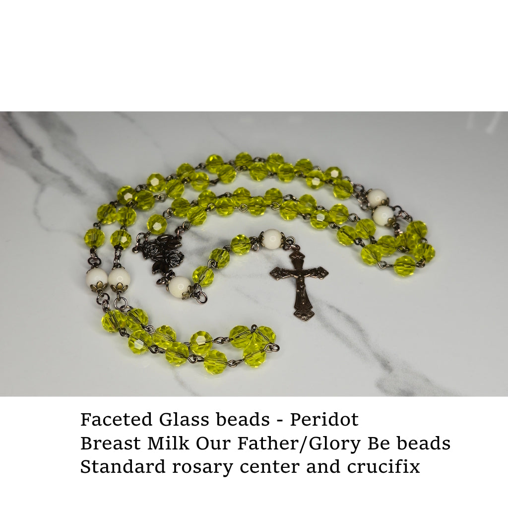 Rosary with peridot-colored faceted glass beads and crucifix on a marble surface