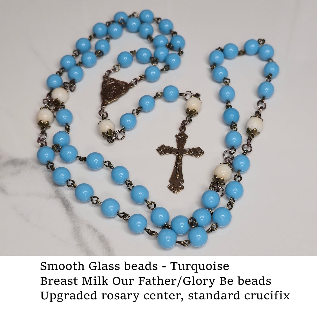 Turquoise-colored glass beadrosary with breast milk Our Father/Glory Be beads on a marble surface