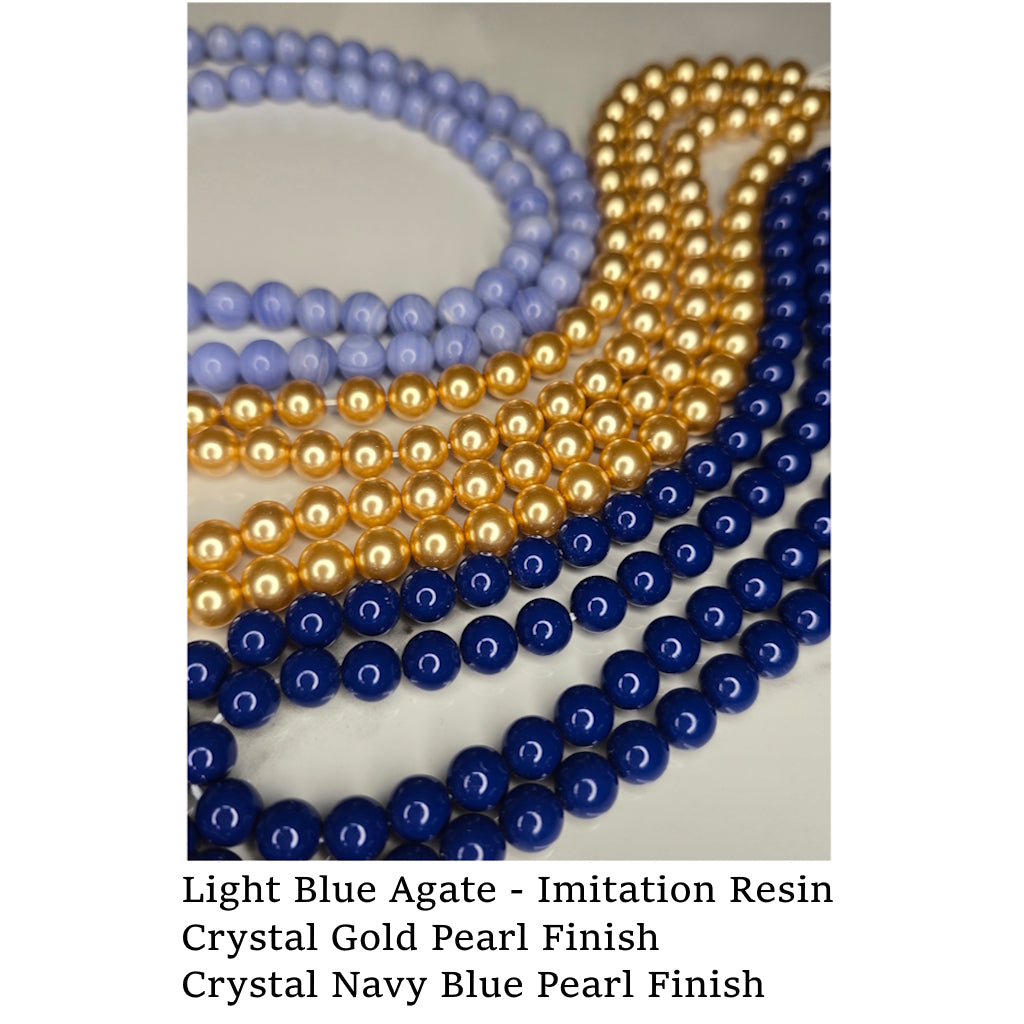 Three bead strands in light blue agate (imitation resin), Crystal gold pearl finish, and crystal navy blue pearl finish on a white surface